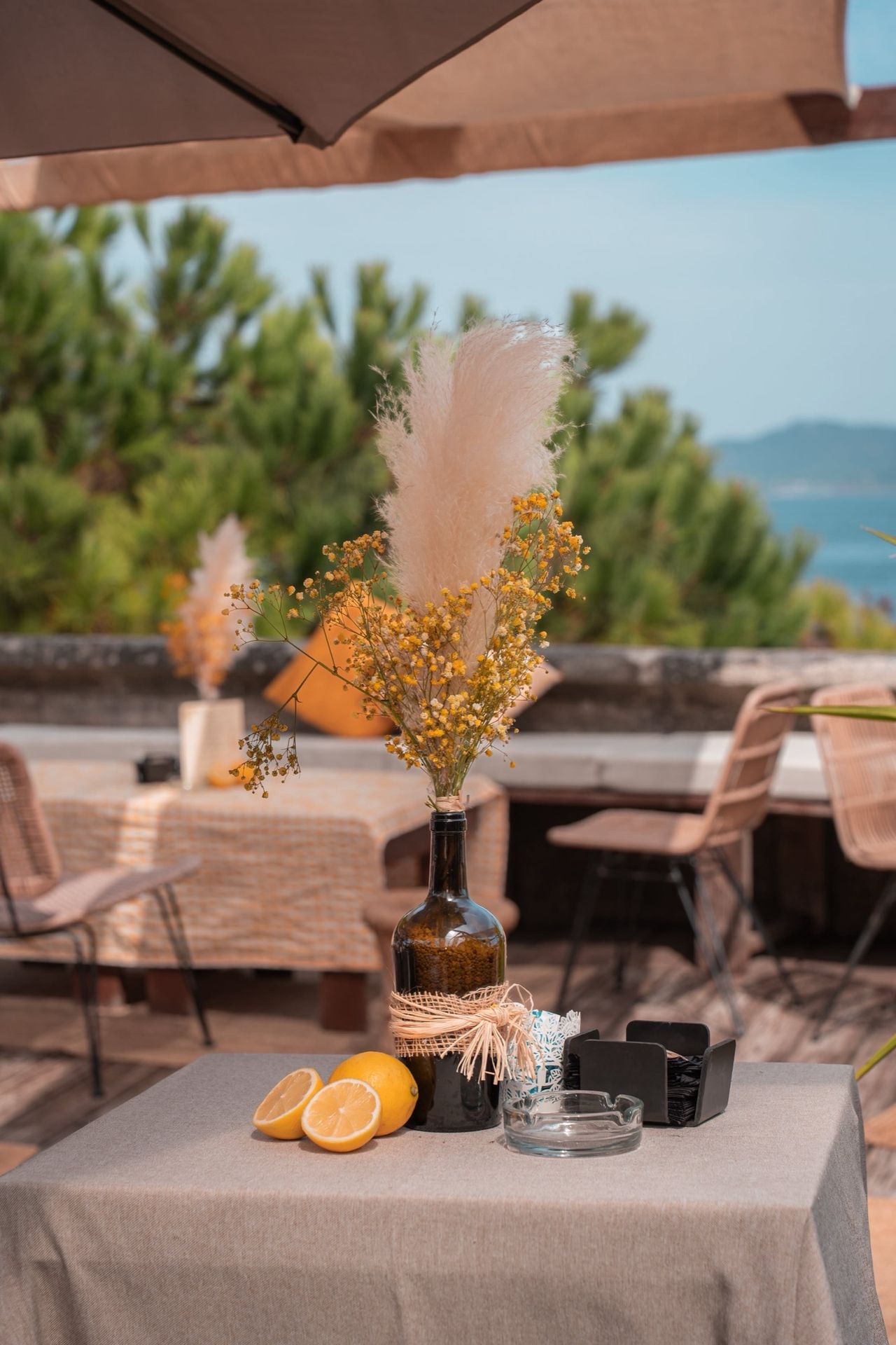 Detalle de mesa decorada con pampas y flores secas, con los pinos y el mar al fondo en Finca Fontaíña