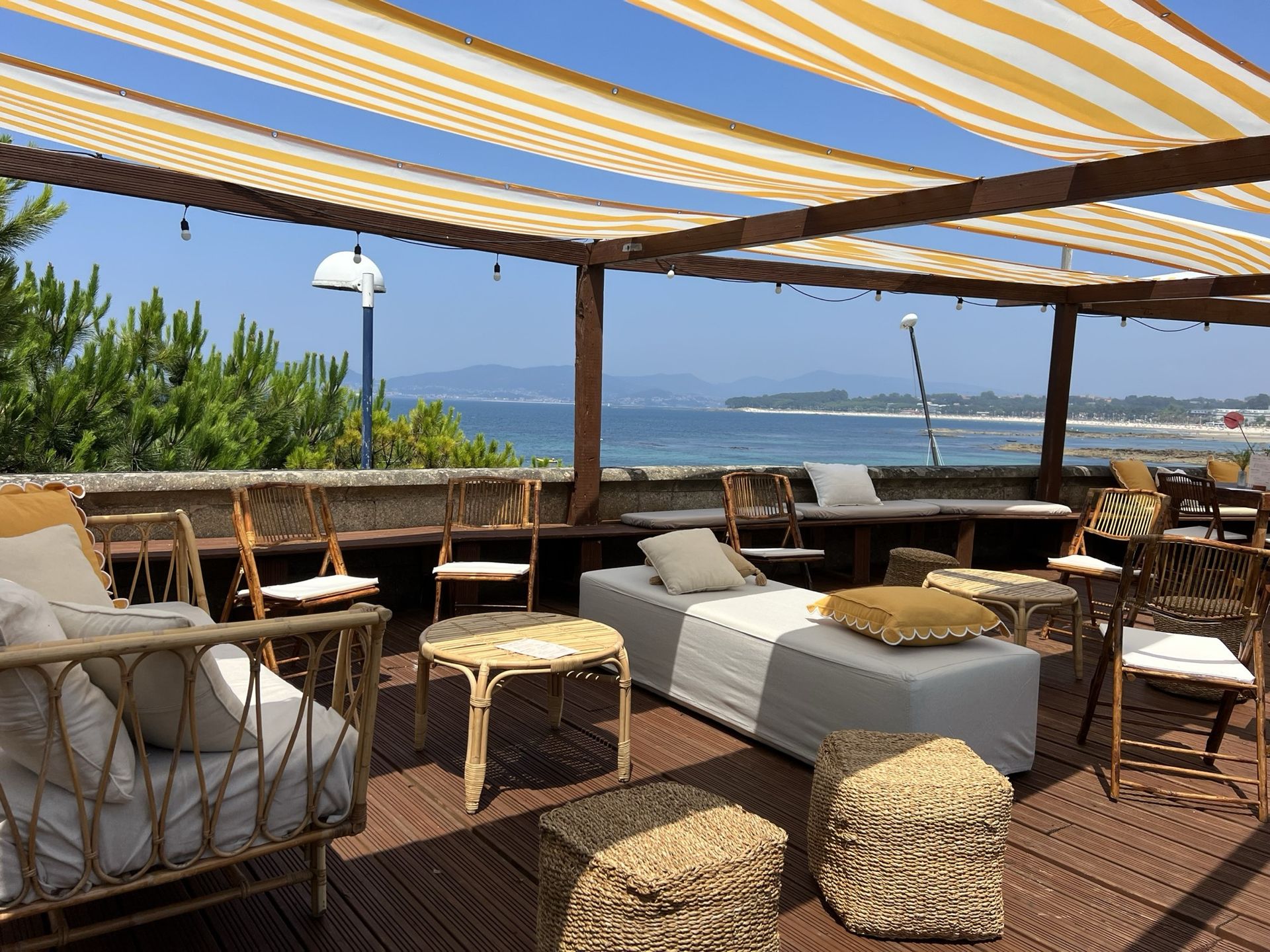 Zona de descanso con sofás de mimbre bajo un toldo de rayas amarillas en la terraza de Finca Fontaíña, frente al mar