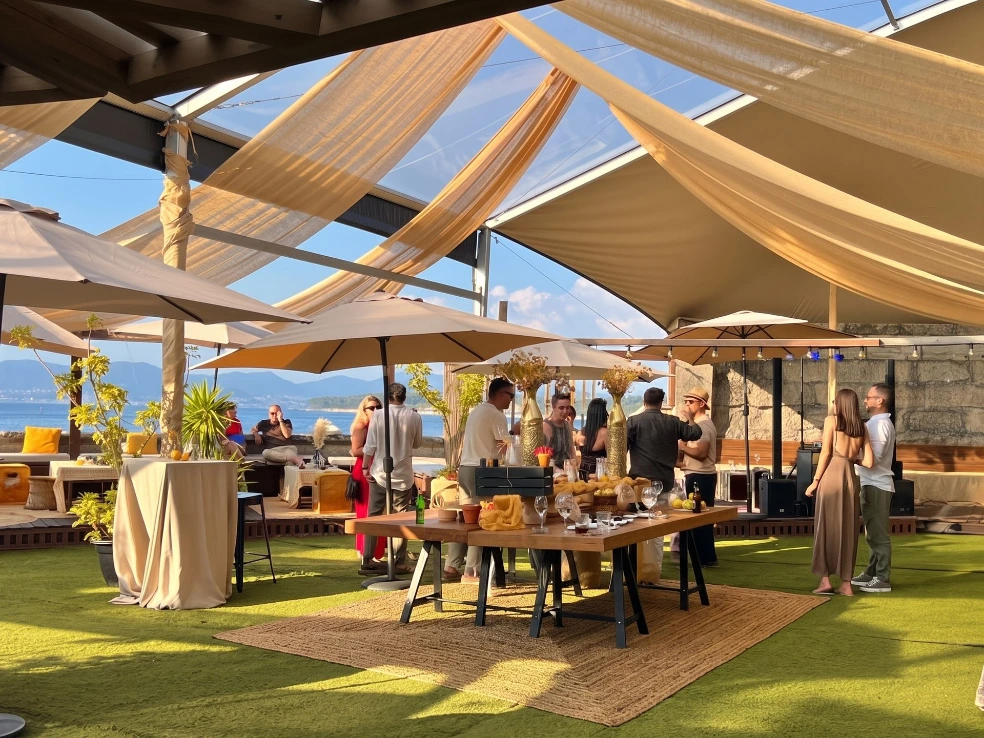 Invitados en el cóctel bajo la carpa transparente con telas y sombrillas, en la terraza de Finca Fontaíña, con la ría de Vigo al fondo